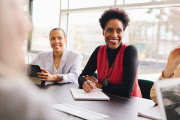 Portrait of cheerful mature black businesswoman listening and smiling with notebook in meeting room