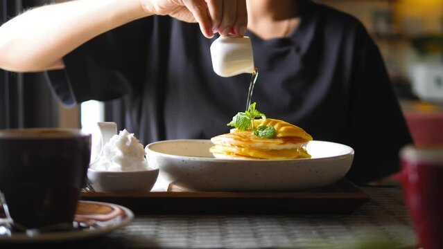 Female pours maple syrup on delicious pancakes. Young woman eating breakfast in vegan restaurant. High quality healthy food 4K footage.
