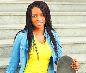 Fototapeta premium Portrait of happy smiling young woman with skateboard wearing vivid yellow hat in the city