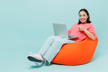 Full body young smiling happy woman of Asian ethnicity 20s wear pink sweater sit in bag chair hold...