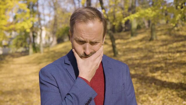A middle-aged handsome Caucasian man thinks about something in a park in fall - closeup - trees in the blurry background
