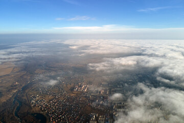 Aerial view from high altitude of distant city covered with puffy cumulus clouds flying by before rainstorm. Airplane point of view of landscape in cloudy weather