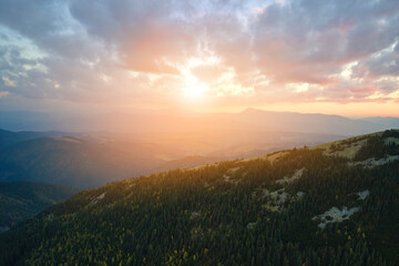 Aerial view of bright foggy morning over dark peak with mountain forest trees at autumn sunrise. Beautiful scenery of wild woodland at dawn