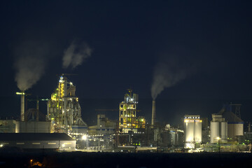 Obraz na płótnie Canvas Illuminated cement plant with high factory structure and tower cranes at industrial production area at night. Manufacture and global industry concept