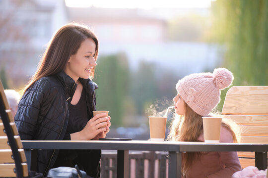 Young mother and her child daughter having good time together sitting at street cafe with hot drinks on sunny fall day. Happiness in family relations concept