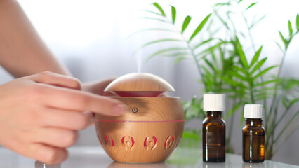 Modern aroma oil diffuser on the white table. Spa concept for body and health care. female is...