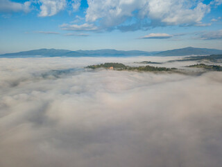 Obraz premium Flight over fog in Ukrainian Carpathians in summer. Mountains on the horizon. A thick layer of fog covers the mountains with a continuous carpet. Aerial drone view.