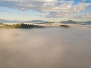 Flight over fog in Ukrainian Carpathians in summer. Mountains on the horizon. A thick layer of fog covers the mountains with a continuous carpet. Aerial drone view.