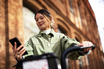 Fototapeta premium Young Chinese woman using the phone. Beautiful happy lady with electric bicycle..
