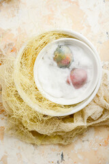 Easter pastel natural eggs on a soft cotton pad in white round bowls with decorations on a textured background. View from above.