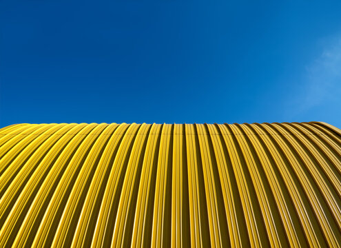 Yellow facade of sheet metal and blue sky from frog perspective. Yellow and blue contrasting on a bright sunny day. Bent roof surface with parallel horizon line, ressembling flag of Ukraine.