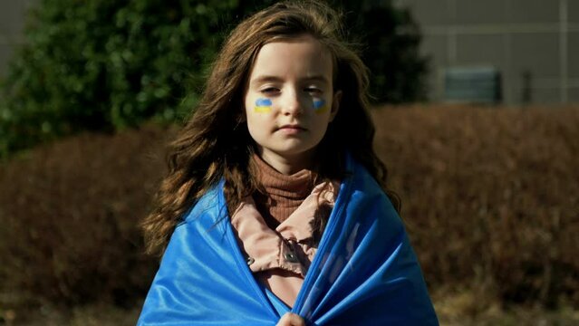 Serious face of a little girl. The child's cheeks are painted with the yellow and blue colors of the Ukrainian flag. Children ask for peace.