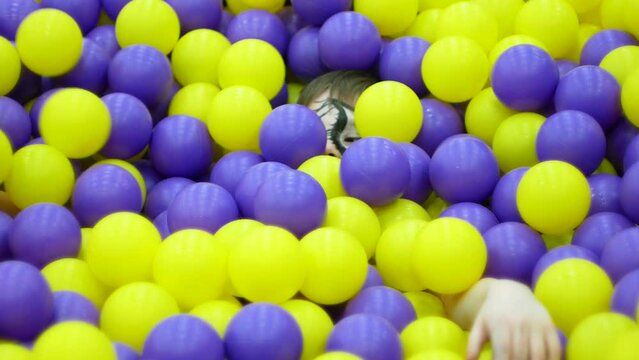 Fun and entertainment for children. Caucasian boy 7-8 years old painted face with aquagrim bathes in colorful balls in an amusement park. Birthday 8 years. Children's attraction