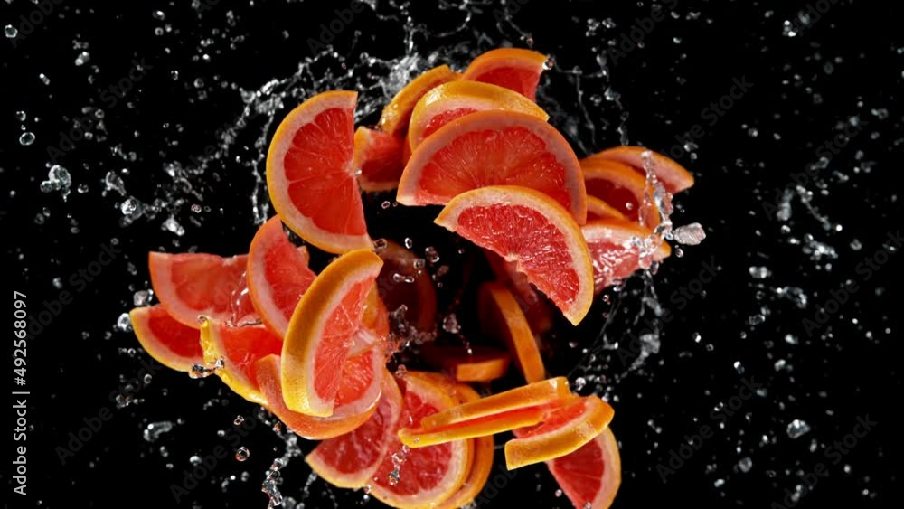Fototapete Super slow motion of rotating grapefruit slices with splashing water, black background. Filmed on high speed cinema camera, 1000 fps. Speed ramp effect.