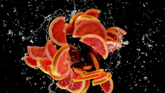Super slow motion of rotating grapefruit slices with splashing water, black background. Filmed on high speed cinema camera, 1000 fps. Speed ramp effect.