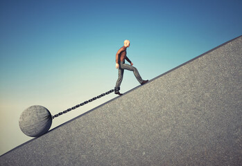 Man walks with a chained foot by a rock.