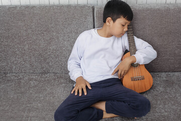 Asian kid in white sweater fall asleep  on the sofa while holding ukulele