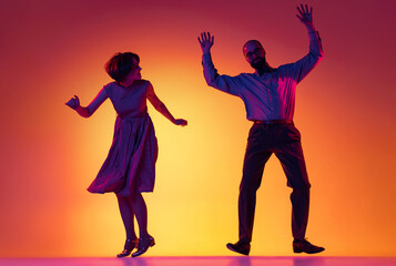 Fototapeta na wymiar Portrait of excited man and woman, couple of dancers in vintage retro style outfits dancing lindy hop dance isolated on gradient yellow and purple background.