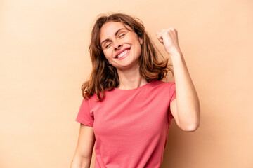 Young caucasian woman isolated on beige background celebrating a victory, passion and enthusiasm,...