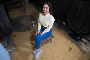 Young beautiful businesswoman sitting on a chair in her wine cellar. The woman is making different expressions and gestures looking at the camera. Enterprising woman concept