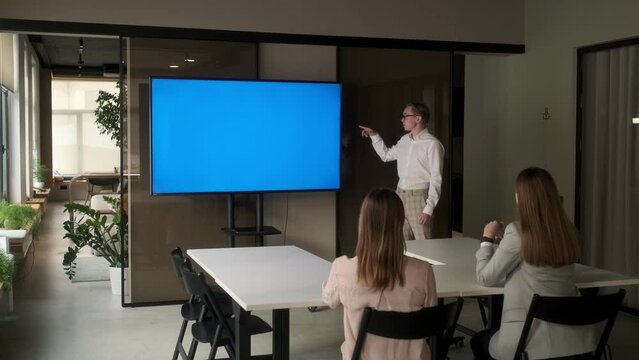Diverse office conference room meeting: male project manager uses Chroma Key wall mounted blue screen TV to present an investment project. Project presentation. The concept of business, training