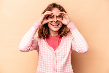 Young caucasian woman isolated on beige background showing okay sign over eyes