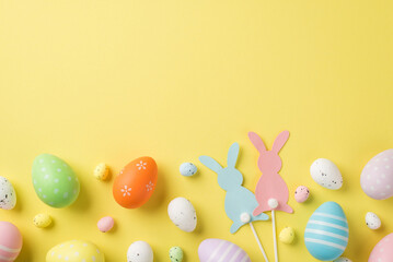 Top view of multicolored Easter eggs and quail ones with two rabbits on sticks situated on the...