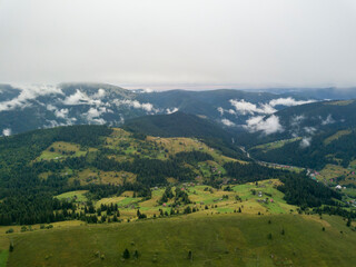 Green slopes of Ukrainian Carpathian mountains in summer. Cloudy morning, low clouds. Aerial drone view.