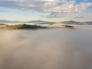 Obraz premium Flight over fog in Ukrainian Carpathians in summer. Mountains on the horizon. A thick layer of fog covers the mountains with a continuous carpet. Aerial drone view.