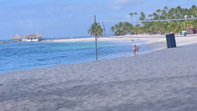 Static wide shot of mother and son walking on the beach beside Caribbean Sea