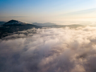Flight over fog in Ukrainian Carpathians in summer. Mountains on the horizon. Aerial drone view.