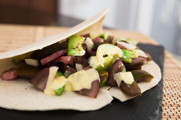 salad of black tomatoes, avocado and onions in Italian tortilla on black stone board
