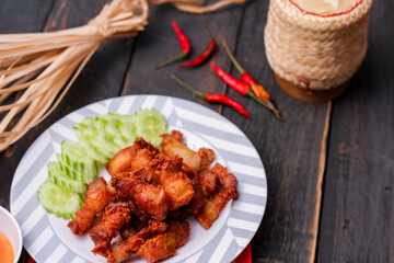 Fried Pork Belly with Fish Sauce and Sticky Rice Served on a white plate on a black wooden floor.