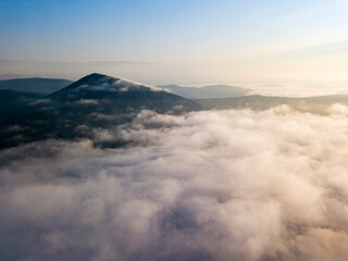 Flight over fog in Ukrainian Carpathians in summer. Mountains on the horizon. Aerial drone view.