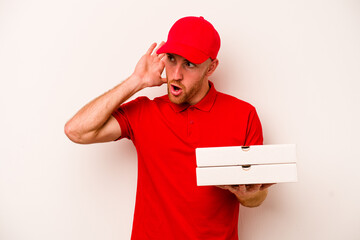 Young delivery caucasian man holding pizzas isolated on white background trying to listening a gossip.