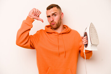 Young caucasian man holding iron isolated on white background showing a dislike gesture, thumbs...