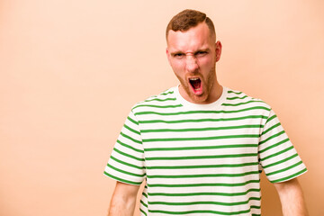 Fototapeta premium Young caucasian man isolated on beige background shouting very angry, rage concept, frustrated.
