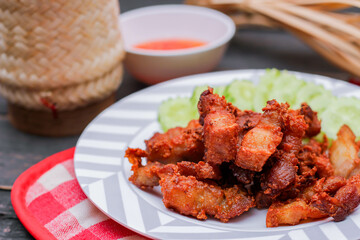 Fried Pork Belly with Fish Sauce and Sticky Rice Served on a white plate on a black wooden floor.