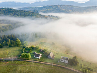 Fototapeta premium Mountain settlement in the Ukrainian Carpathians in the morning mist. Aerial drone view.