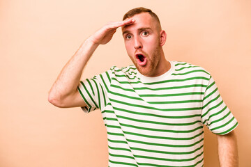 Young caucasian man isolated on beige background shouts loud, keeps eyes opened and hands tense.