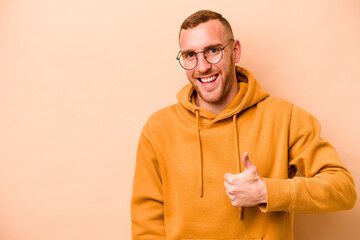 Naklejka premium Young caucasian man isolated on beige background smiling and raising thumb up
