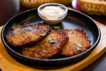 Fried grated potato pancakes with sour cream on frying pan