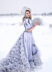 Young blonde woman in light blue vintage ball gown and decorated head piece standing in winter...