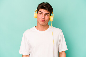 Young caucasian man listening to music isolated on blue background dreaming of achieving goals and...