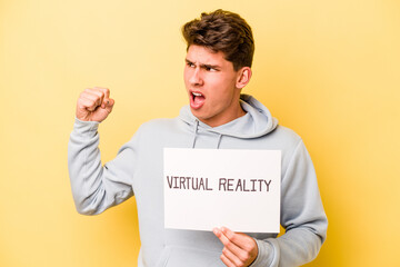 Young caucasian man holding virtual placard isolated on yellow background raising fist after a victory, winner concept.