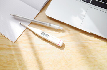 家で体温計で検温する。パソコンと筆記具