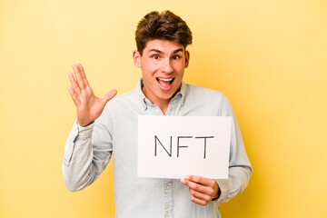 Young caucasian man holding NFT placard isolated on yellow background receiving a pleasant...