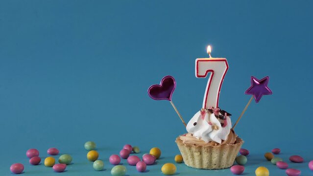 Happy birthday greetings to a 7 year old child, birthday cupcake with candles and birthday decorations on a blue background. Copy space.place for text