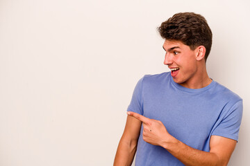 Young caucasian man isolated on white background points with thumb finger away, laughing and carefree.