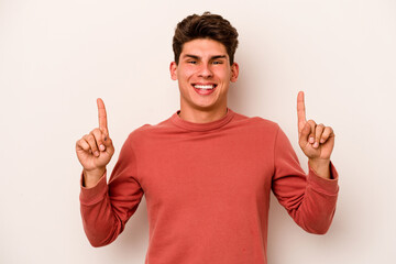Young caucasian man isolated on white background indicates with both fore fingers up showing a...